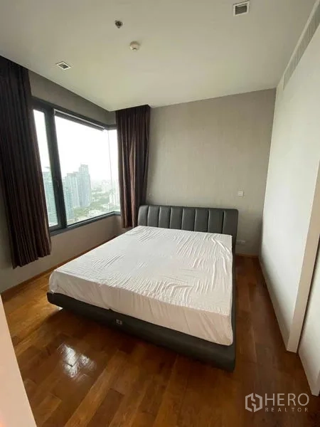 Condominium for rent or sale in Khlong Toei, Bangkok - Corner bedroom with large windows, city views, upholstered bed and wood flooring.