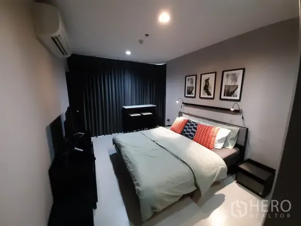 Condominium for rent or sale in Khlong Toei, Bangkok - Master bedroom with king bed, wall-mounted reading lights, dark curtains and framed artwork above the headboard.
