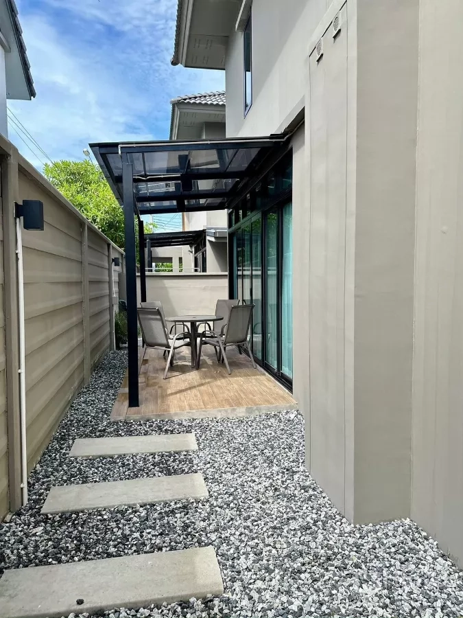 Detached House for rent in Samut Prakan - Side garden patio with glass canopy, outdoor table set and gravel path.
