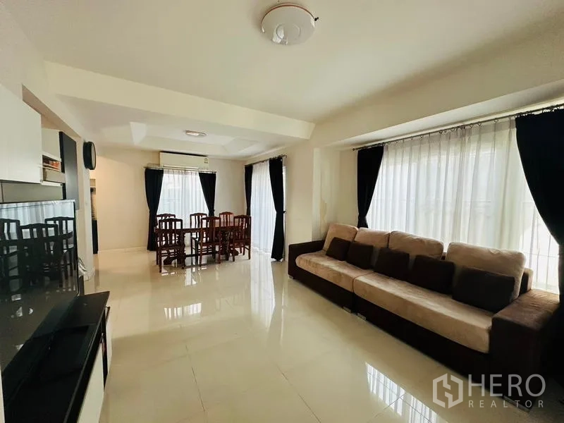 Detached House for sale in Prawet, Bangkok - Bright living and dining room with large sofa, full-height windows and blackout curtains.