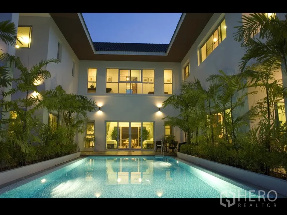 Detached House for rent in Khan Na Yao, Bangkok - Modern two-storey detached house in Khan Na Yao with an illuminated private pool courtyard and palm landscaping at dusk.