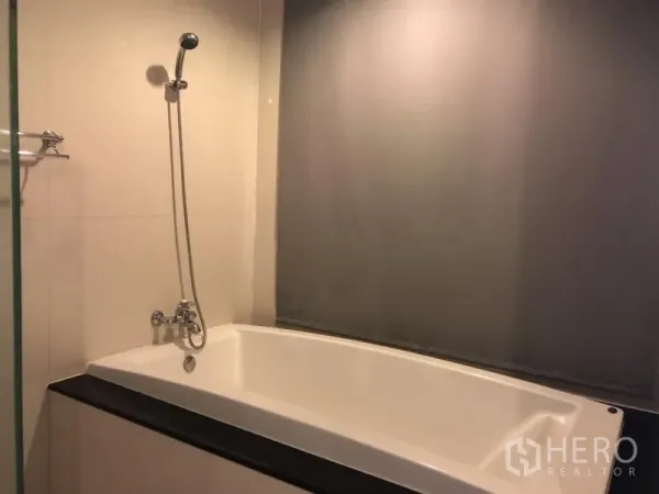 Condominium for rent in Pathum Wan, Bangkok - Bathroom with a built-in bathtub and handheld shower against tiled walls.