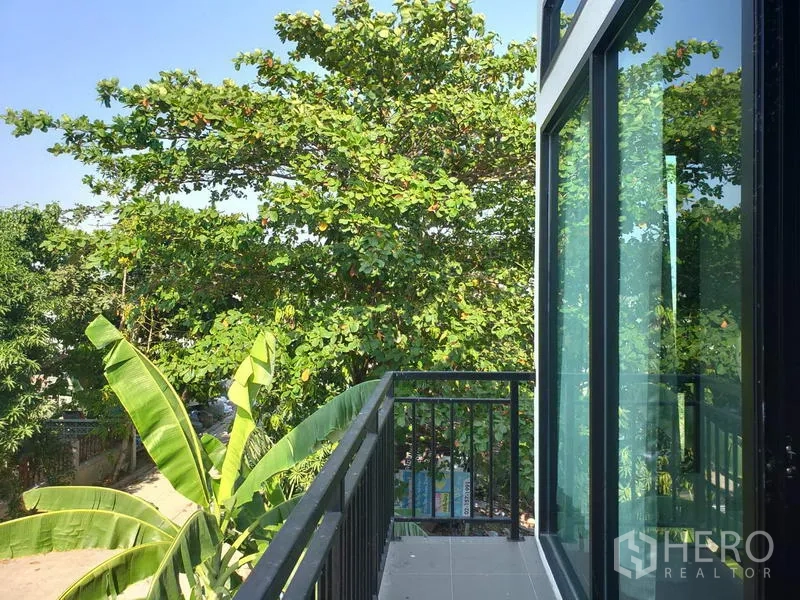 Factory for rent or sale in Lam Luk Ka, Pathum Thani - Small balcony with black metal railing and glass sliding doors overlooking green trees.