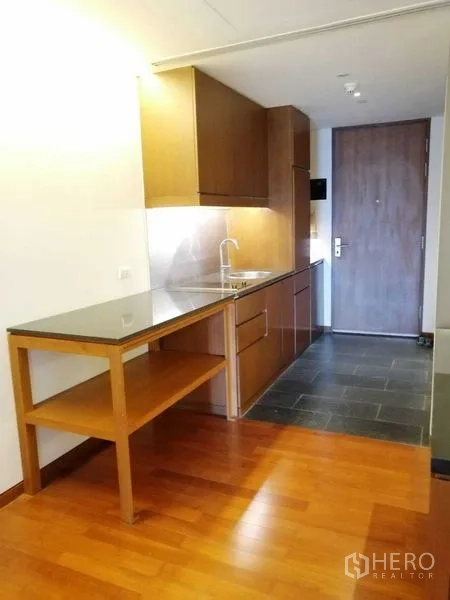 Condominium for rent in Pathum Wan, Bangkok - Entry corridor leading to kitchenette with built-in storage and wood floors.