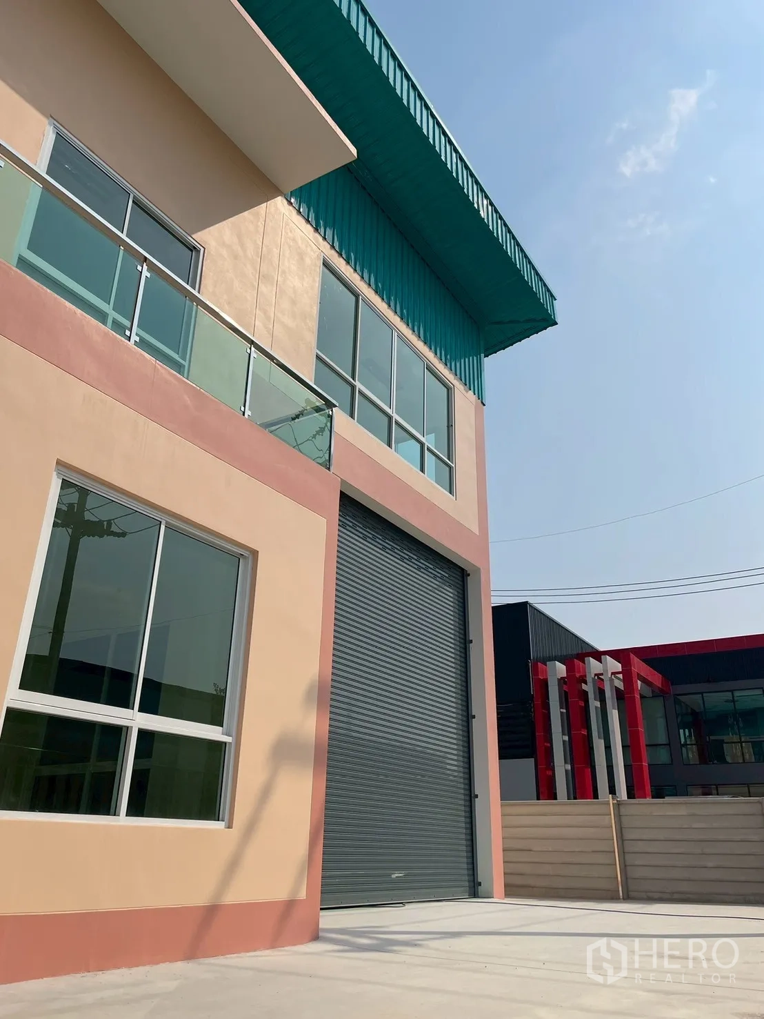 Factory for sale in Sam Phran, Nakhon Pathom - Modern factory exterior with teal roof, big electric roller shutter, and upper balcony.
