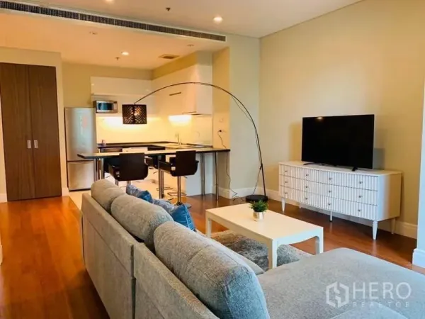 Condominium for rent in Khlong Toei, Bangkok - Lounge with TV console facing a sofa, adjoining kitchen and breakfast bar in an airy layout.