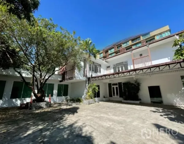 Home Office for rent in Watthana, Bangkok - Two-storey white home office with balconies around a spacious tree-lined courtyard under a blue sky.