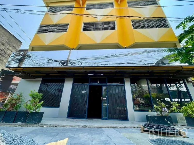 Shophouse for rent in Lat Phrao, Bangkok - Four-storey yellow and gray shophouse exterior with glass frontage and planters in Lat Phrao, Bangkok.