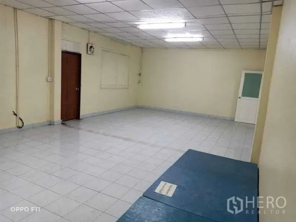 Warehouse for rent or sale in Mueang Samut Sakhon, Samut Sakhon - Large tiled multipurpose room with fluorescent lighting and a wooden door.