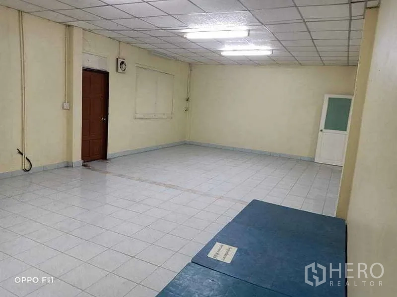 Warehouse for rent or sale in Mueang Samut Sakhon, Samut Sakhon - Large tiled multipurpose room with fluorescent lighting and a wooden door.