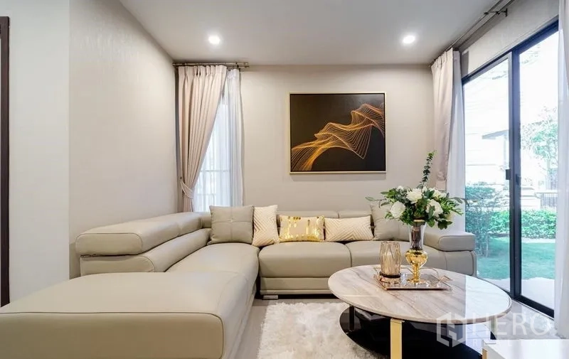 Detached House for sale in Lam Luk Ka, Pathum Thani - Cozy lounge area with L-shaped sofa by garden-facing glass doors.