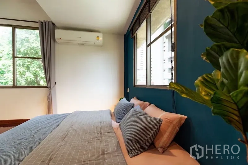 Townhouse for rent in Watthana, Bangkok - Sunlit bedroom with blue wall, double windows and air-conditioning.