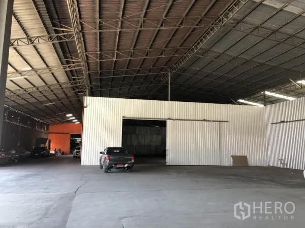 Warehouse for rent in Nong Chok, Bangkok - Spacious warehouse interior with high steel-truss roof, corrugated metal partitions, and wide concrete loading floor with vehicle access.