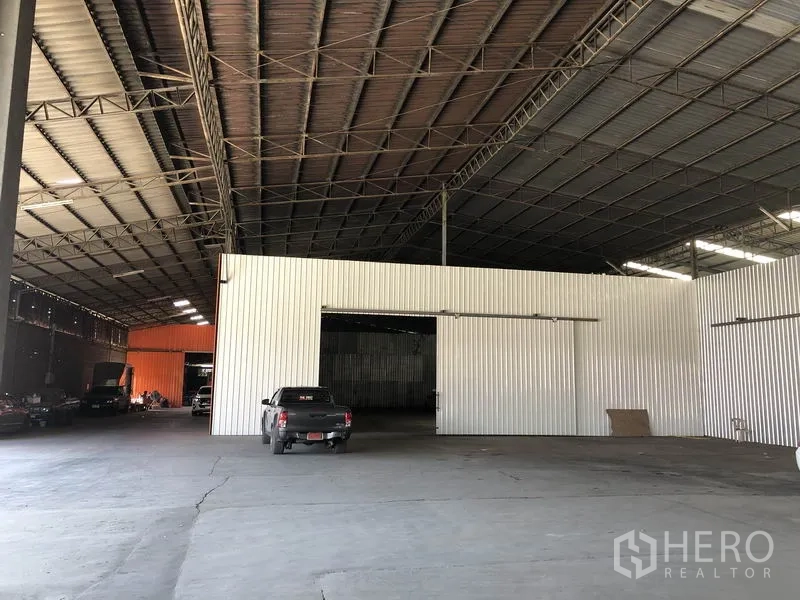 Warehouse for rent in Nong Chok, Bangkok - Spacious warehouse interior with high steel-truss roof, corrugated metal partitions, and wide concrete loading floor with vehicle access.