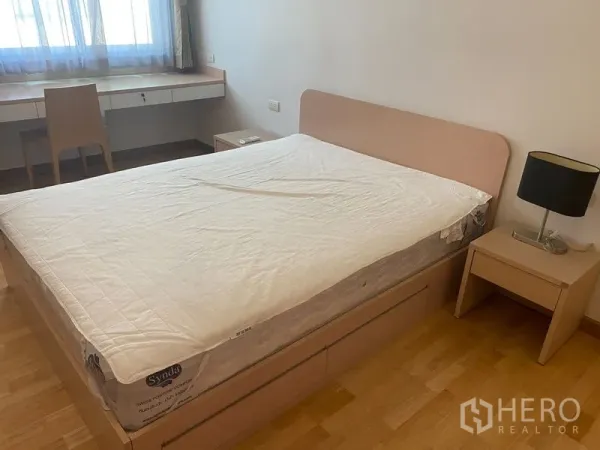 Condominium for rent or sale in Khlong Toei, Bangkok - Master bedroom with double bed, bedside table and built-in desk beneath a window.