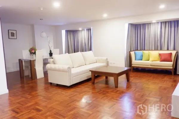 Condominium for rent in Khlong Toei, Bangkok - Open-plan living and dining area with two sofas, coffee table and floor-to-ceiling curtains.