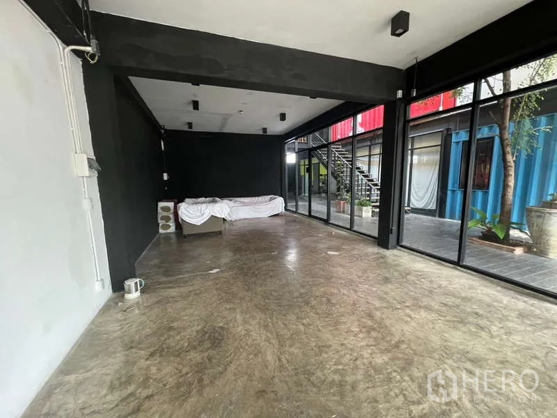 Retail Space for rent - Corner interior with windows on two sides, black walls, concrete floor and trees visible outside.