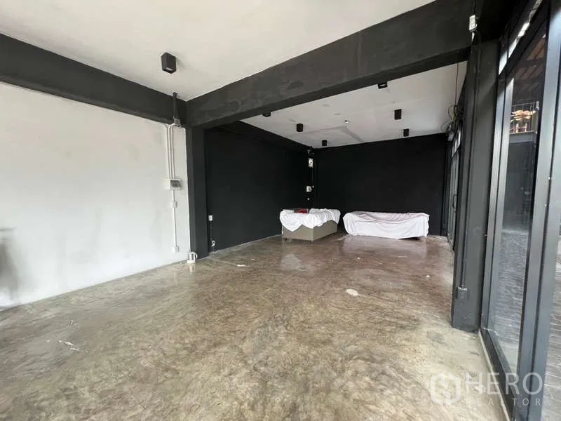 Retail Space for rent - Empty rectangular retail space with black-and-white walls, ceiling fixtures and a glass frontage to the corridor.