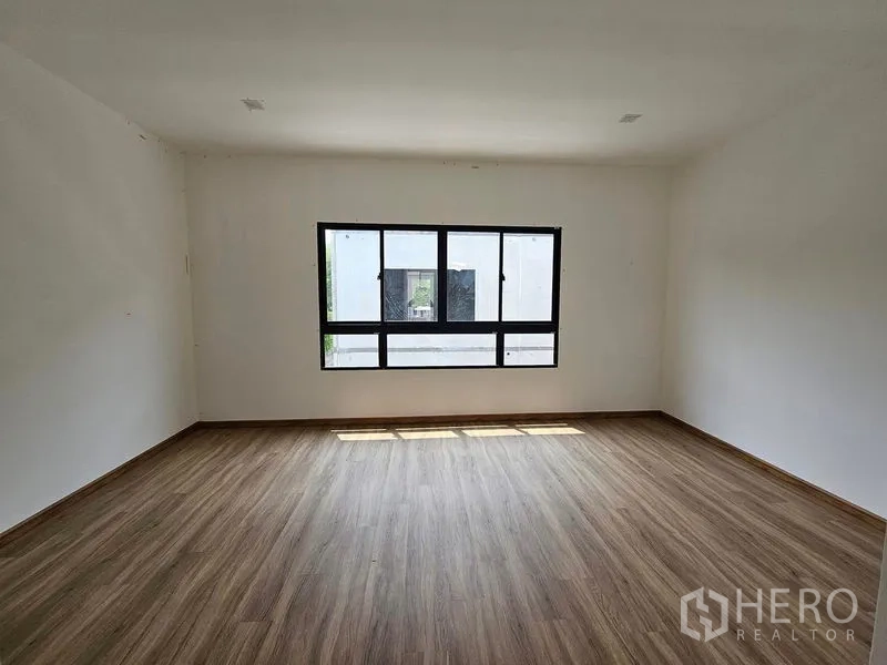 Townhouse for rent in Bang Kapi, Bangkok - Large bedroom with wood-look flooring and a wide horizontal window bringing in natural light.