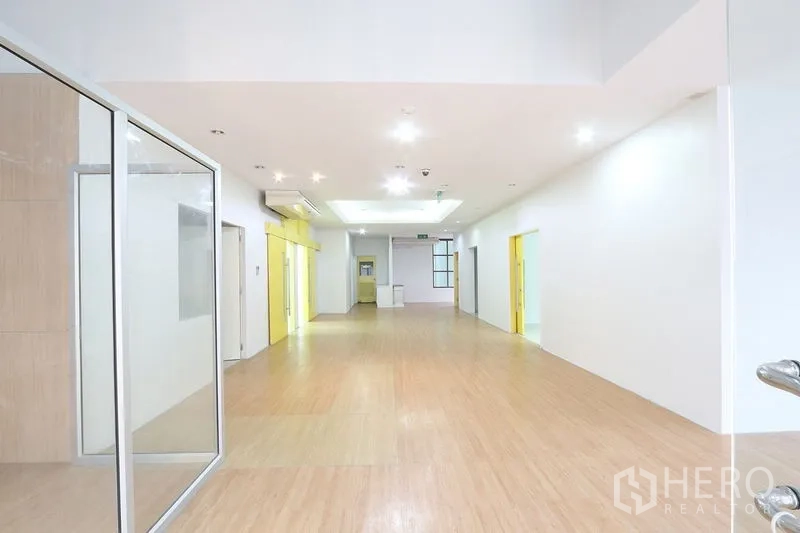 Office Space for rent in Bang Na, Bangkok - Bright open‑plan corridor with wood flooring, recessed lights and glass partitions ready for meeting rooms.