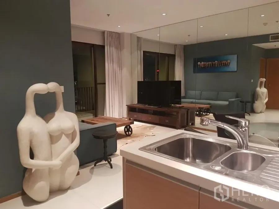 Condominium for rent or sale in Khlong Toei, Bangkok - Open-plan living room with mirrored wall, TV console and balcony doors, seen from a kitchen sink in a Sukhumvit condo.