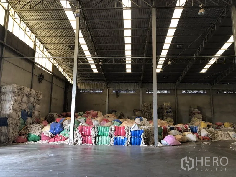 Factory for rent in Bang Bua Thong, Nonthaburi - Deep warehouse aisle with strip skylights and stacked materials along both walls.