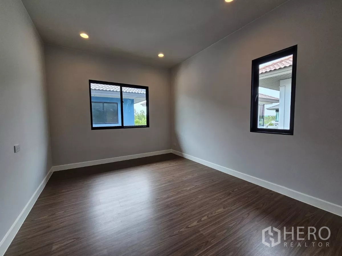 Detached House for sale in Lam Luk Ka, Pathum Thani - Another sunlit bedroom with dual-aspect windows and wood floor.
