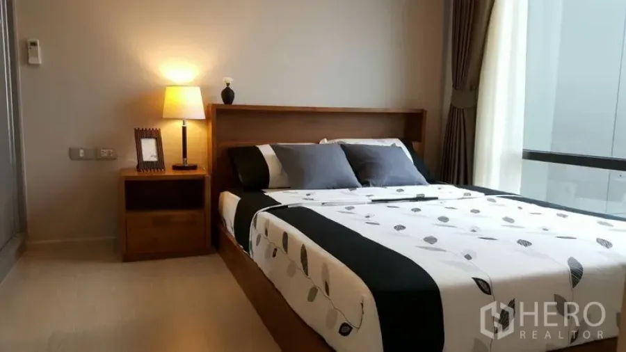 Condominium for rent in Khlong Toei, Bangkok - Cozy bedroom with double bed, bedside lamp and large window with curtains.