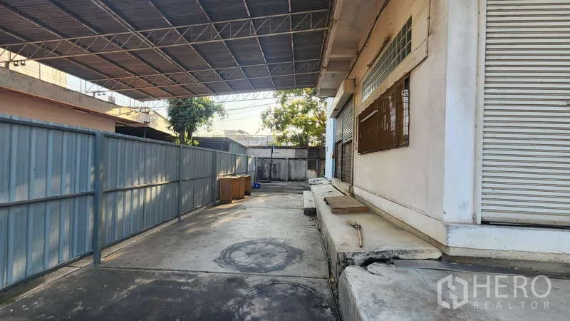 Factory for rent in Chom Thong, Bangkok - Covered loading dock with roller shutters along the building facade.
