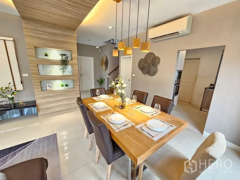 Detached House for rent in Prawet, Bangkok - Dining room facing kitchen doorway with warm wood accents and pendant lights.