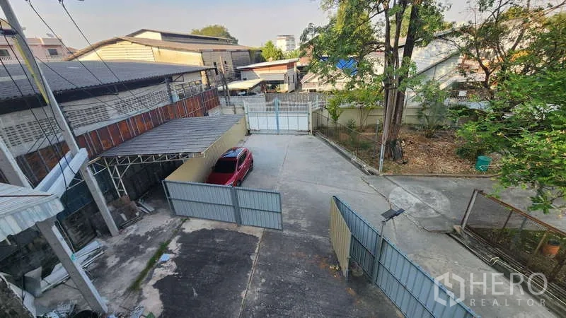 Factory for rent in Chom Thong, Bangkok - Gated driveway and parking yard viewed from an upper floor.