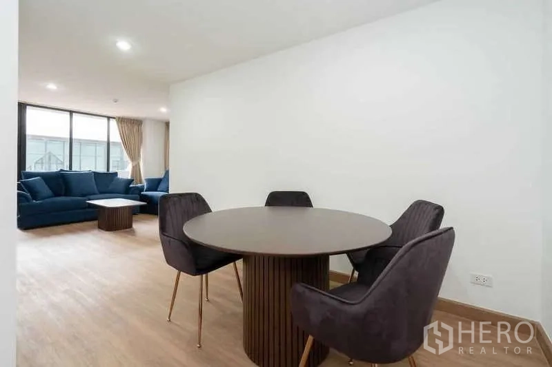 Apartment for rent in Khlong Toei, Bangkok - Open-plan dining and living space with blue sofas and large windows.