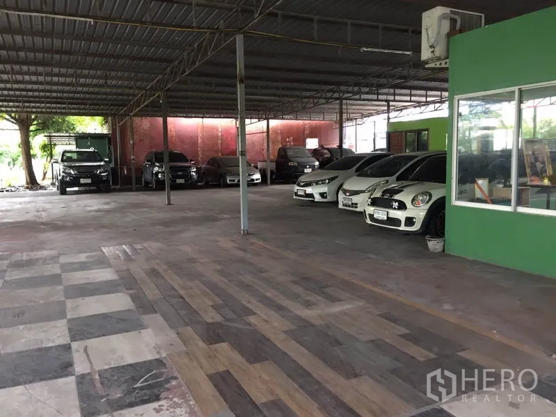 Warehouse for rent in Pathum Thani - Sheltered warehouse parking area with tiled floor beside a green office unit.