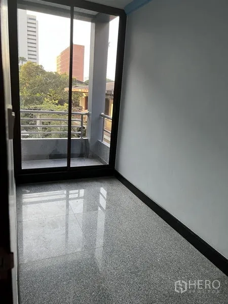 Home Office for rent in Pathum Wan, Bangkok - Compact room with polished floors and sliding glass doors opening to a balcony and greenery.