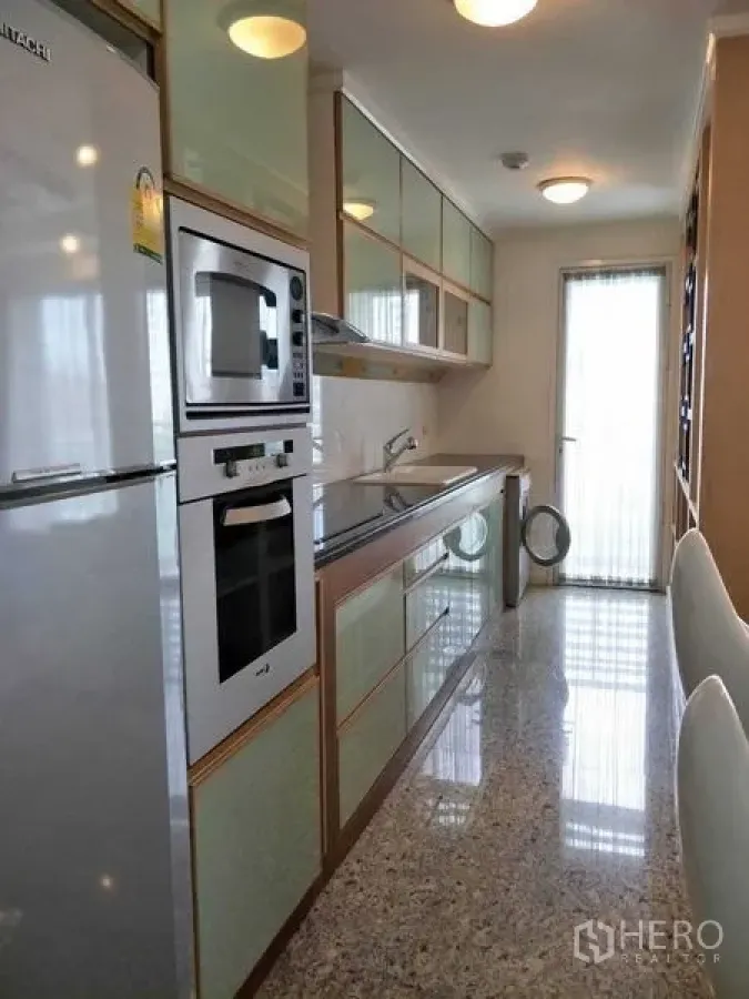 Condominium for rent or sale in Watthana, Bangkok - Galley kitchen with mint glass cabinets, built-in oven and balcony door in an Ekkamai condo, Watthana, Bangkok.