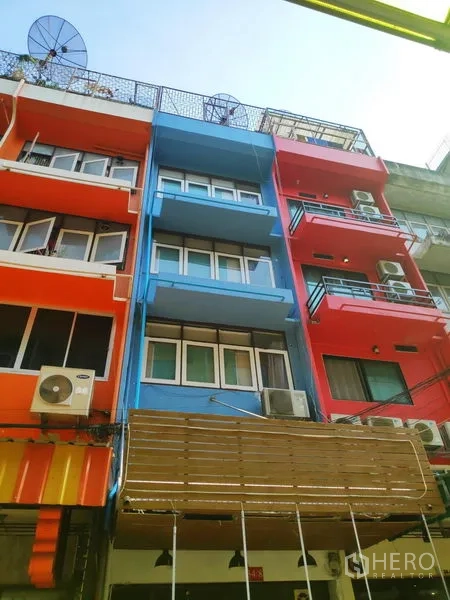 ทาวน์เฮาส์ ให้เช่าในSathon, Bangkok - ภาพมุมเงยของทาวน์เฮ้าส์สีฟ้าระหว่างอาคารสีแดงและสีส้มที่อยู่ข้างเคียง