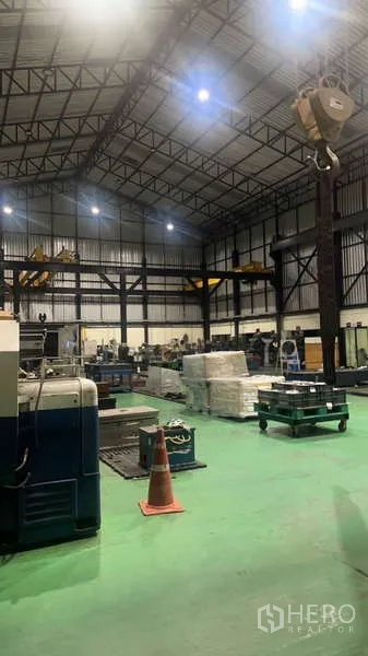 Factory for sale in Si Racha, Chon Buri - Evening view of workshop showing hoist, equipment and pallets under bright lights.