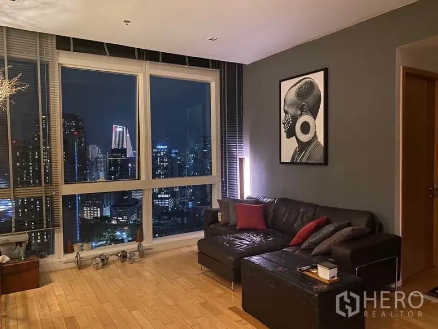 Condominium for rent in Khlong Toei, Bangkok - Seating area beside floor‑to‑ceiling windows offering dramatic night city views.