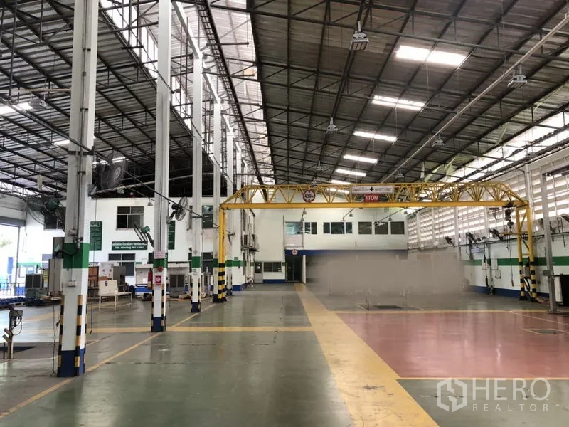 Factory for rent in Lam Luk Ka, Pathum Thani - Open production hall with tall columns, ventilated side walls and a yellow gantry crane spanning the bay near internal offices.
