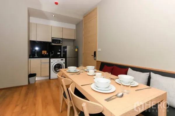 Condominium for rent in Khlong Toei, Bangkok - Six-seat dining table laid with tableware beside the kitchenette and entry door.