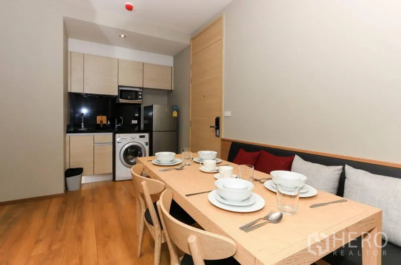 Condominium for rent in Khlong Toei, Bangkok - Six-seat dining table laid with tableware beside the kitchenette and entry door.