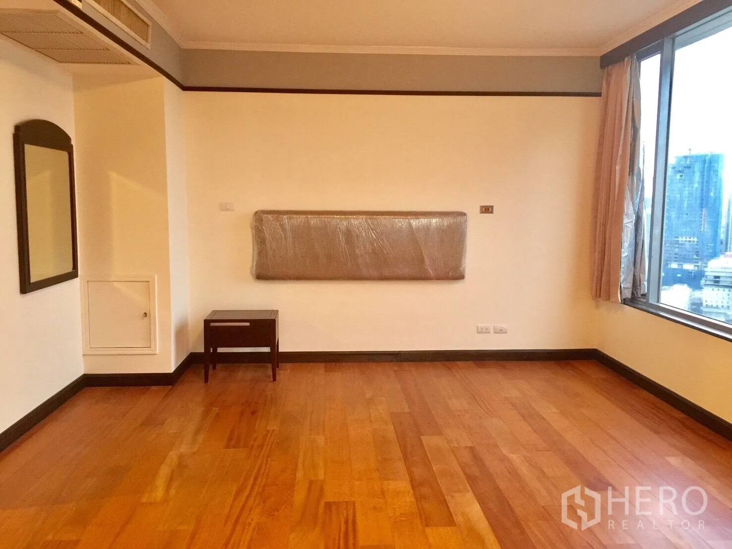 Condominium for rent in Pathum Wan, Bangkok - Large bedroom with corner windows showcasing skyline views and wooden floors.
