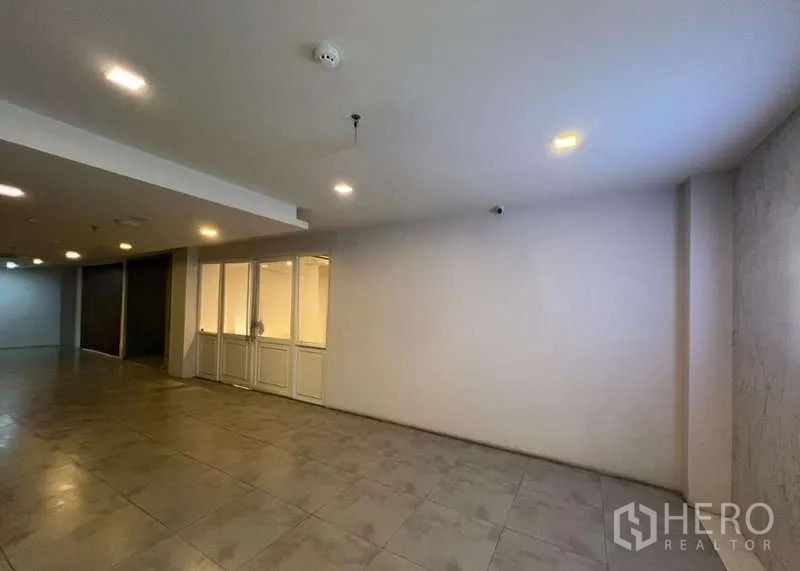 Retail Space for rent - Building corridor outside the unit showing tiled flooring and recessed ceiling lights.