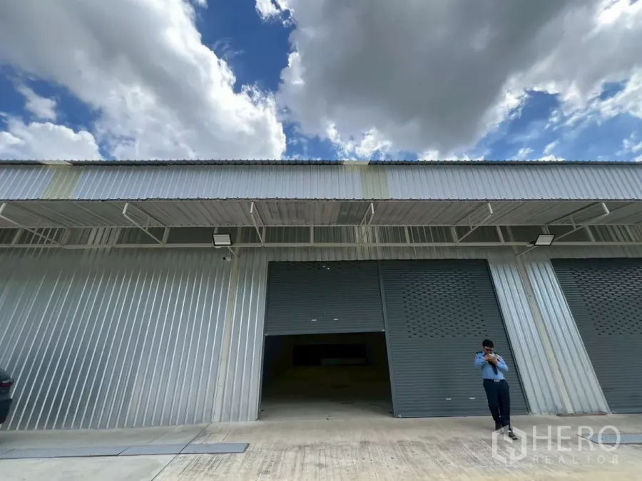Warehouse for rent in Min Buri, Bangkok - Modern metal-clad warehouse facade with twin gray roller shutters and a covered loading bay within an industrial compound.