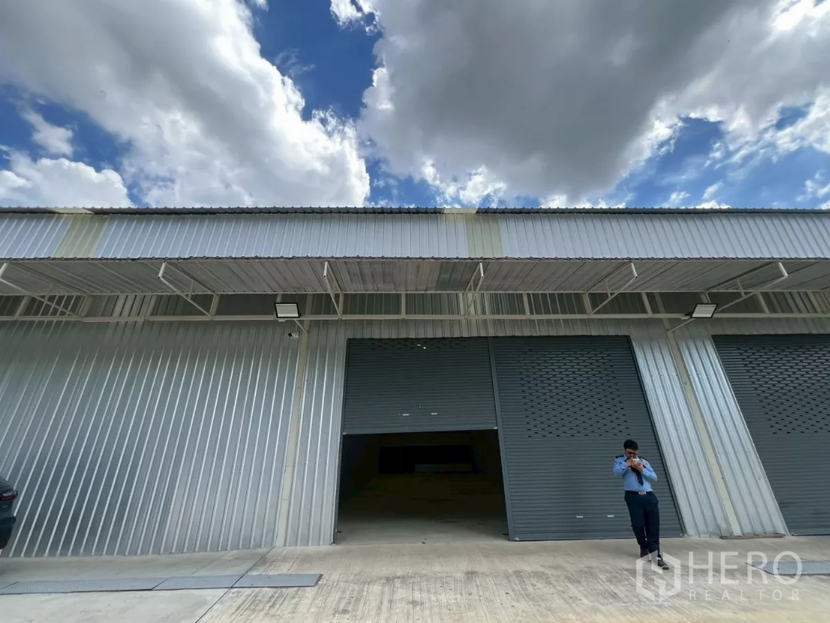 Warehouse for rent in Min Buri, Bangkok - Modern metal-clad warehouse facade with twin gray roller shutters and a covered loading bay within an industrial compound.