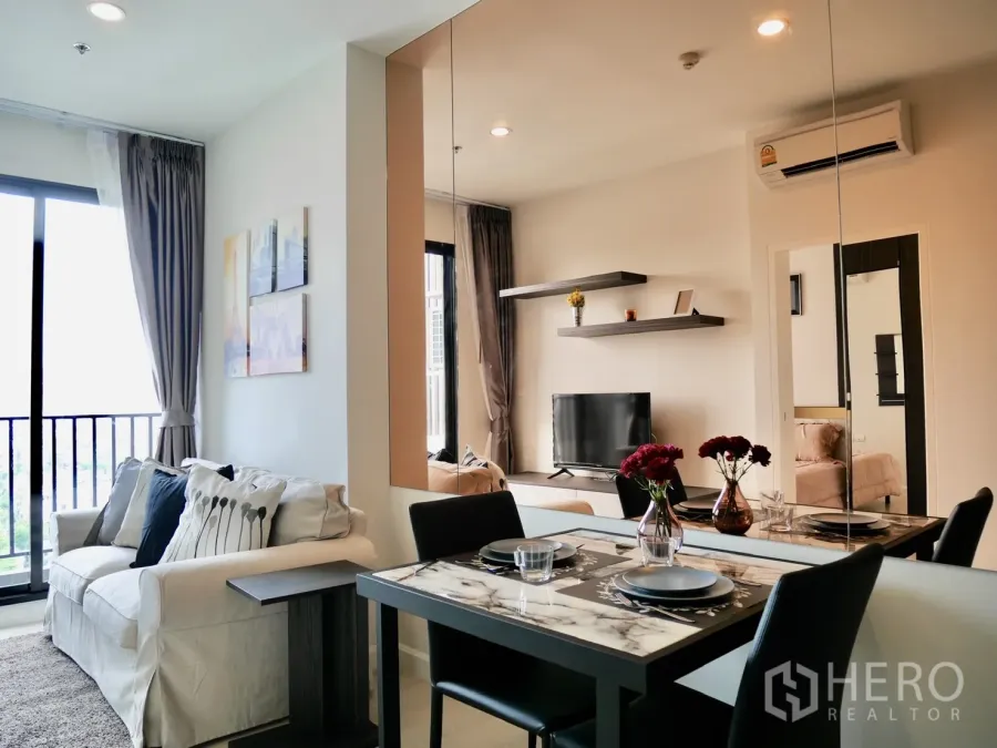 Condominium for rent in Pathum Wan, Bangkok - Bright living and dining area with sofa, marble-top table, wall shelves and mirror beside a balcony.
