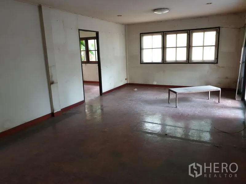 Detached House for rent or sale in Watthana, Bangkok - Spacious living area with multiple windows, light walls and red-toned parquet flooring.
