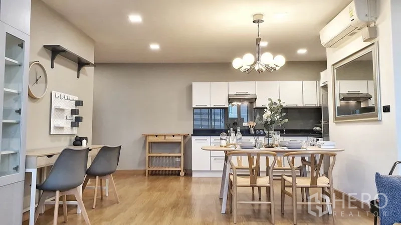 Condominium for rent in Khlong Toei, Bangkok - Kitchen and dining zone with white cabinets, glass-front cupboards and a wooden dining set under a chandelier.