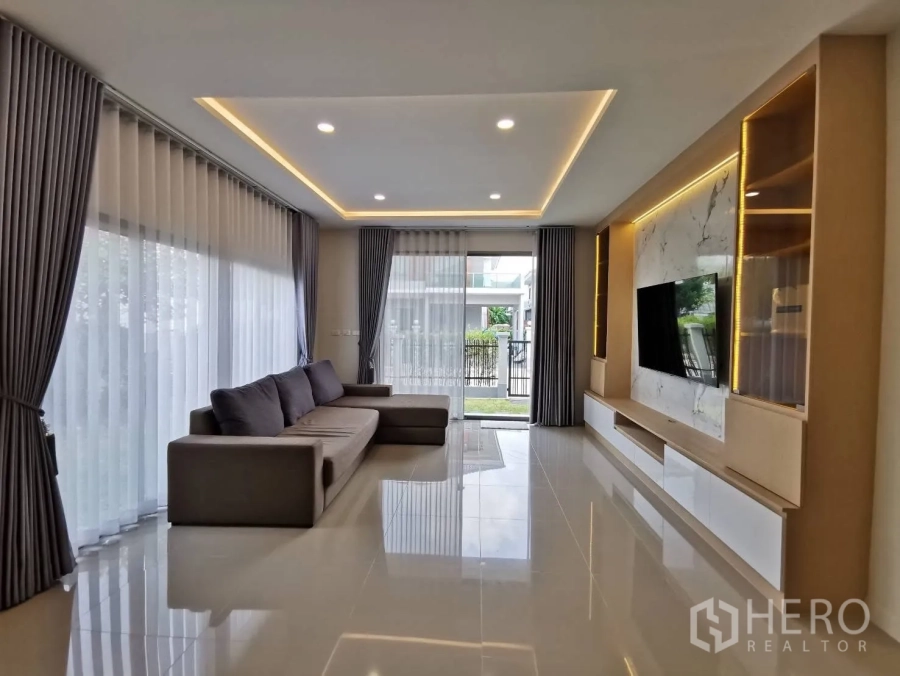 Detached House for rent in Bang Phli, Samut Prakan - Spacious living room with L-shaped sofa, large windows, and a built-in TV wall.