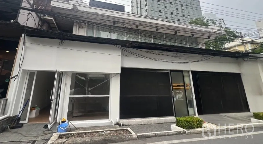 Retail Space for rent in Watthana, Bangkok - Street-facing retail shopfront in Thonglor with a white facade, large glazing and shutters, and a low-rise building set against a high-rise backdrop.